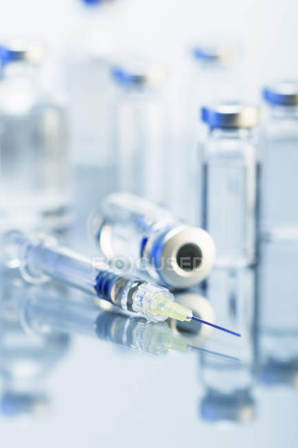 Medizinische Einweg-Spritze aus Kunststoff umgeben von versiegelten Medikamentenflaschen — Stockfoto