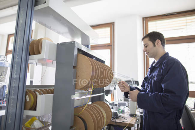 Eletricista masculino puxando cabo de alimentação do tambor de cabo na oficina — Fotografia de Stock