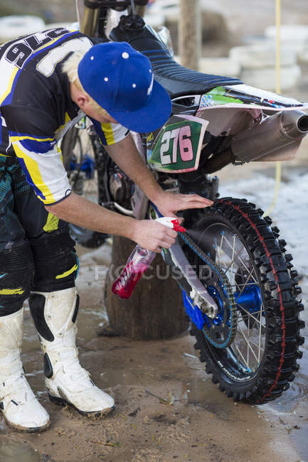 Young male motocross competitor leaning forward and cleaning motorcycle — Stock Photo