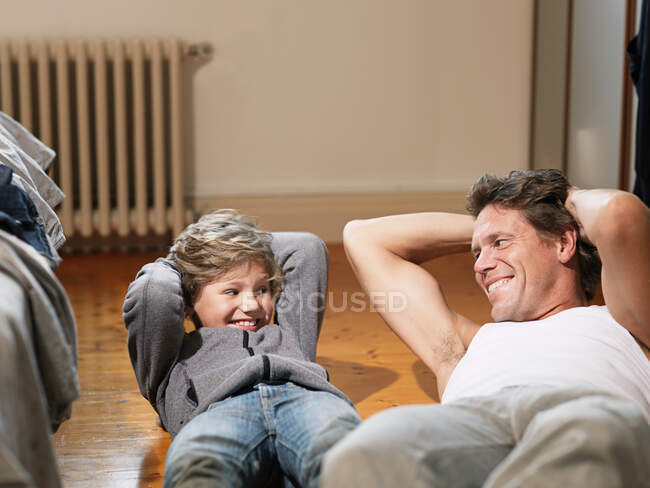 Hombre maduro e hijo realizando ejercicios en el dormitorio - foto de stock