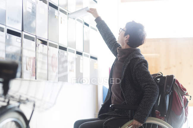 Woman in wheelchair, reaching up, posting mail through letterbox — Stock Photo