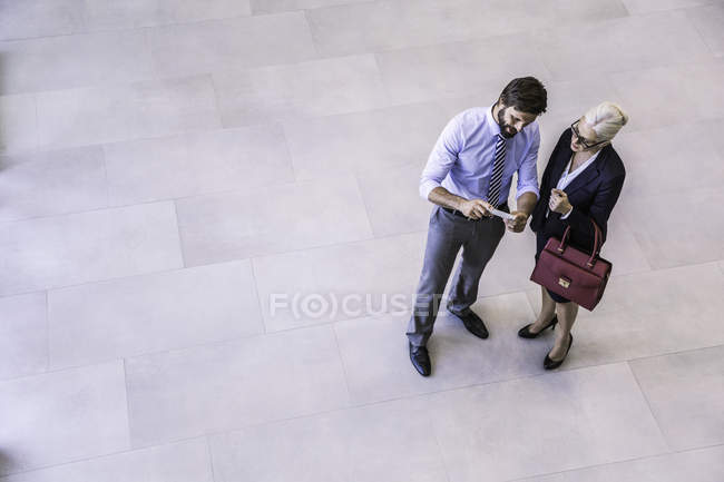 High angle view of two businessman and woman reading smartphone text in office atrium — Stock Photo