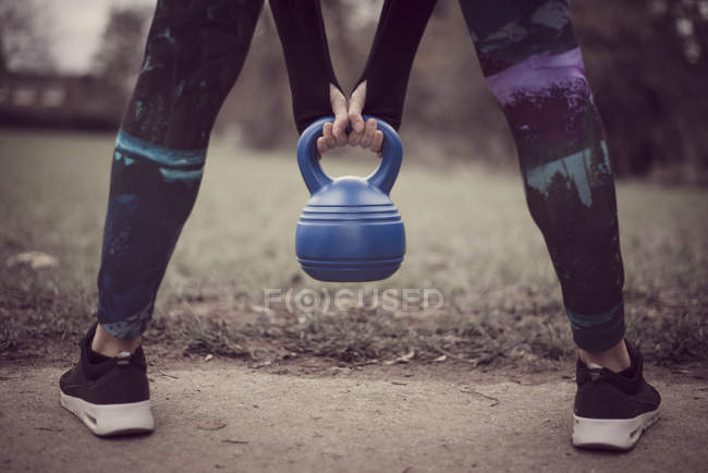Rear view of womans low section, open legged holding kettle bell — Stock Photo