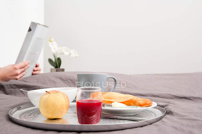 Plateau de petit déjeuner au lit et personne lisant le journal sur fond — Photo de stock