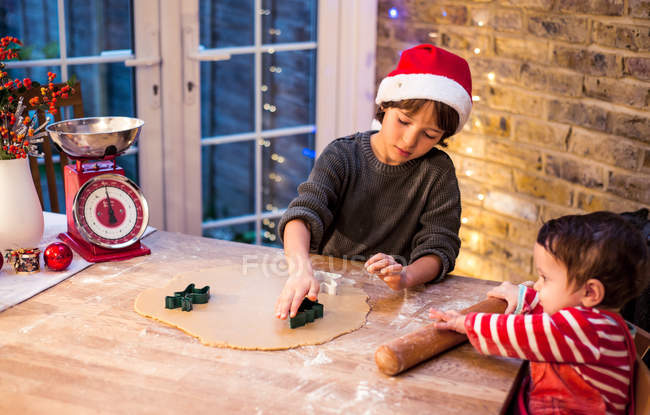 Boy preparing Christmas cookies with baby brother at kitchen counter — Stock Photo