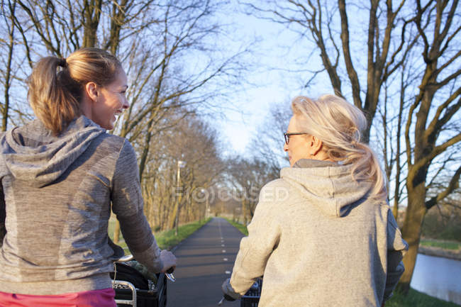 Visão traseira das mulheres cara a cara ciclismo na estrada arborizada — Fotografia de Stock