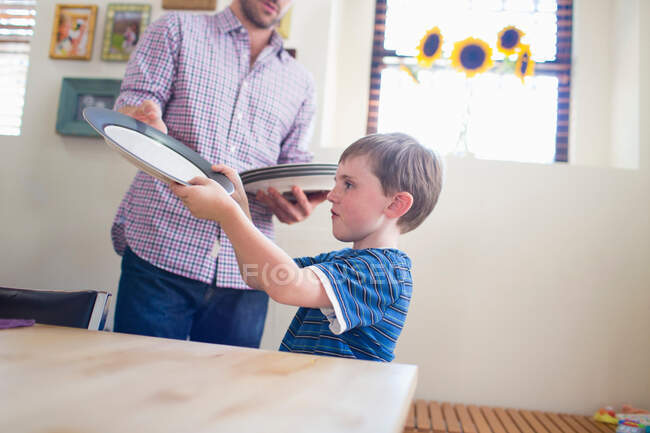 Hijo poniendo la mesa con padre - foto de stock