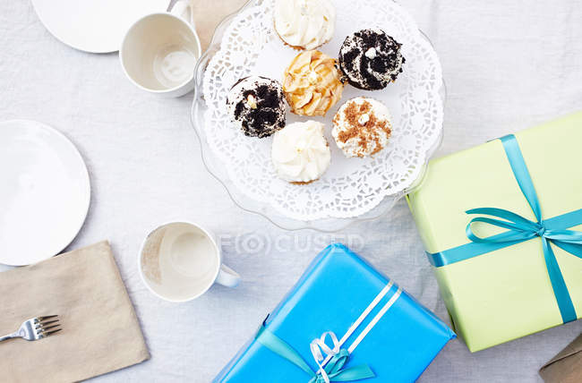 Cupcakes, presentes de aniversário e louças na mesa — Fotografia de Stock