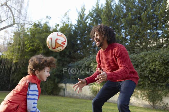 Padre e hijo jugando con el fútbol en el jardín sonriendo - foto de stock