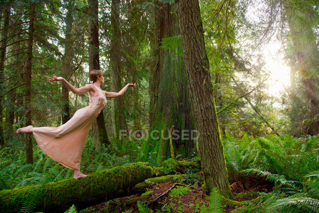 Зрелая женщина, стоящая на бревне в лесу — стоковое фото