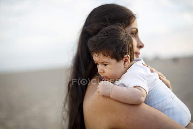 Закрытие матери, стоящей на пляже с младенцем — стоковое фото