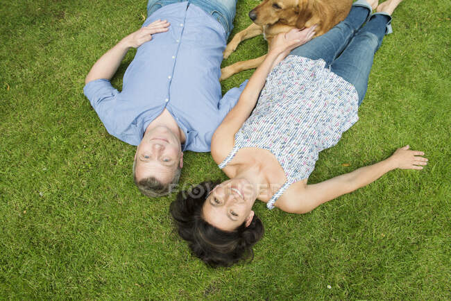 Retrato de casal maduro deitado na grama com o cão — Fotografia de Stock