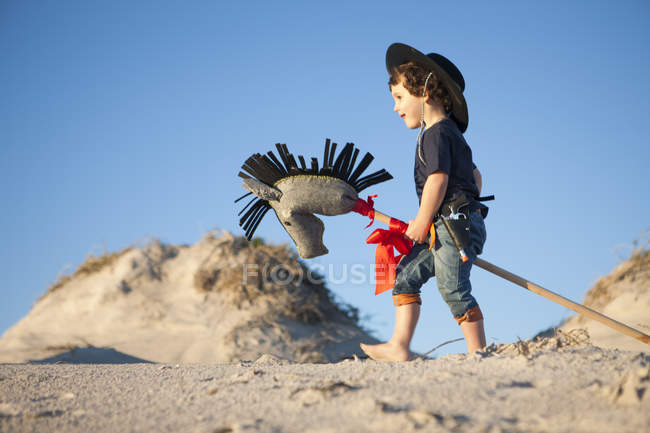 Хлопчик одягнений як ковбой з хобі кінь у піщаних дюнах — стокове фото