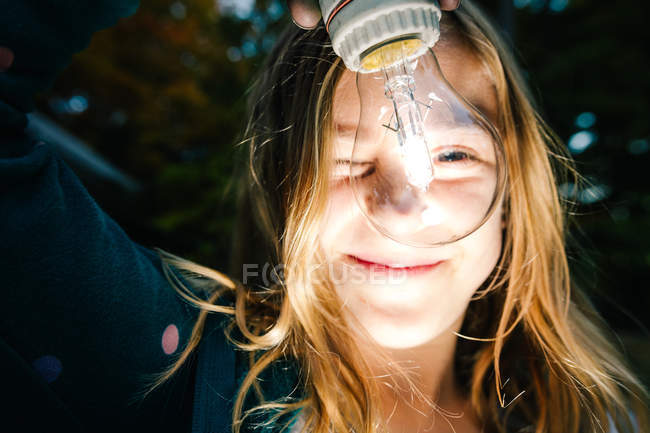Portrait of girl holding illuminated lightbulb in garden at dusk — Stock Photo