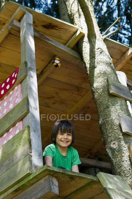 Улыбающийся мальчик сидит в домике на дереве — стоковое фото