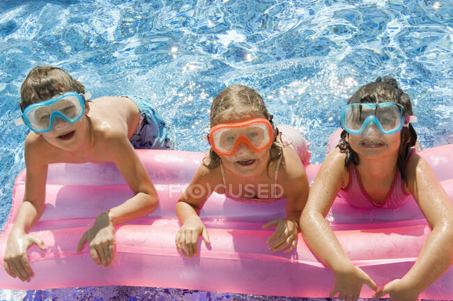 Trois enfants sur un gonflable dans une piscine — Photo de stock
