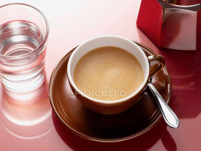 Cup of coffee with spoon and glass of water on table — Stock Photo