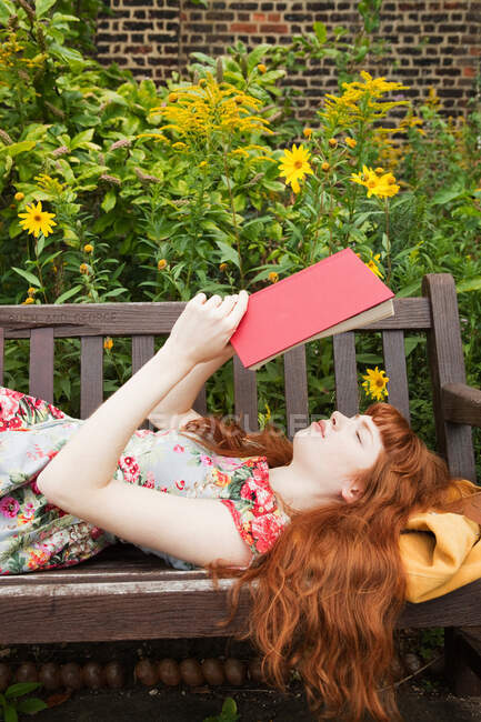 Жінка лежить на паркбенчі, читає книгу — стокове фото