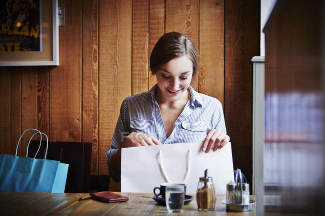 Giovane donna seduta in un caffè in cerca di shopping bag — Foto stock