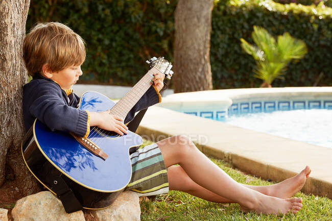 Niño tocando la guitarra en la piscina - foto de stock