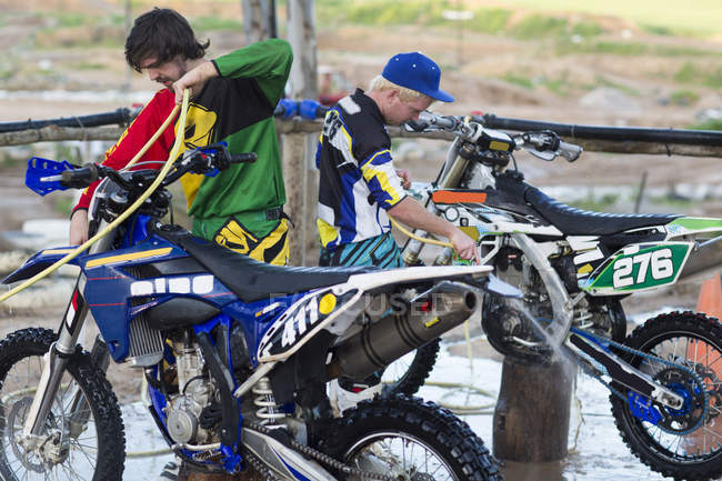 Dois competidores de motocross masculino limpando motocicletas com mangueiras de água — Fotografia de Stock