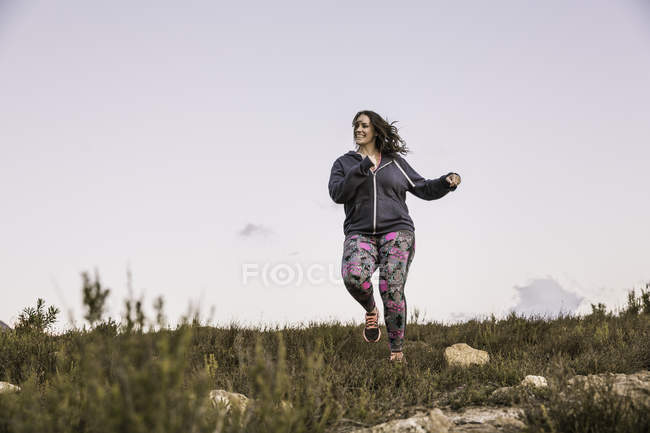 Full length front view of plus size woman jogging downhill — Stock Photo