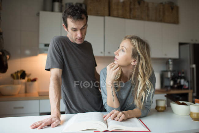 Livro de receitas de leitura de casal na cozinha — Fotografia de Stock
