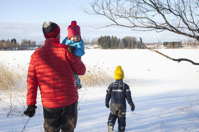 Padre y dos hijos caminando en el paisaje cubierto de nieve, vista trasera - foto de stock
