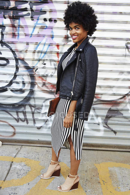 Retrato urbano de una joven blogger de moda con pelo afro por graffiti wall, Nueva York, EE.UU. - foto de stock