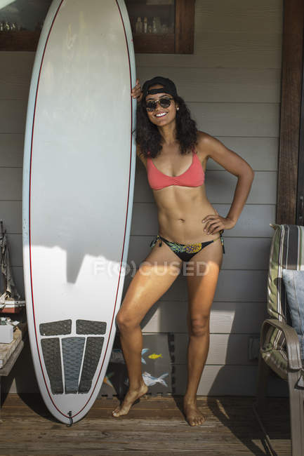 Portrait of young surfing woman standing on porch, Rockaway Beach, New York State, USA — стокове фото