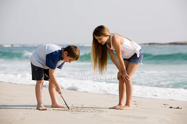 Chica y niño dibujando en la arena - foto de stock