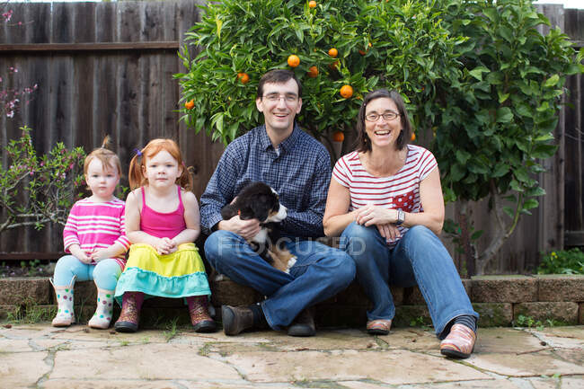 Portrait of young family with dog, sitting in garden — Stock Photo