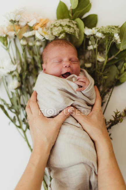 Mother placing swaddled newborn baby daughter on flowers — Stock Photo