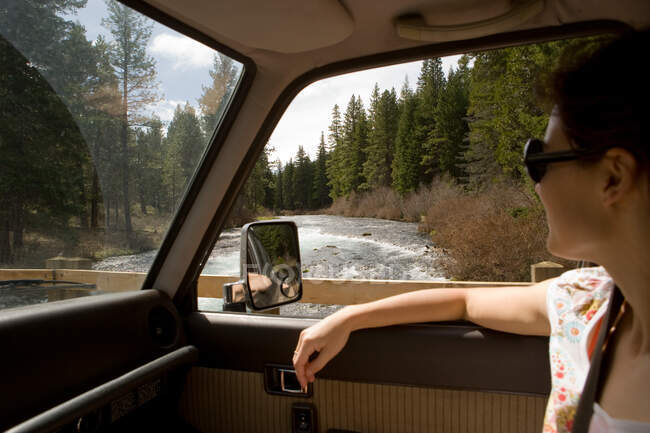 Woman looking through car window at forest scenery — Stock Photo