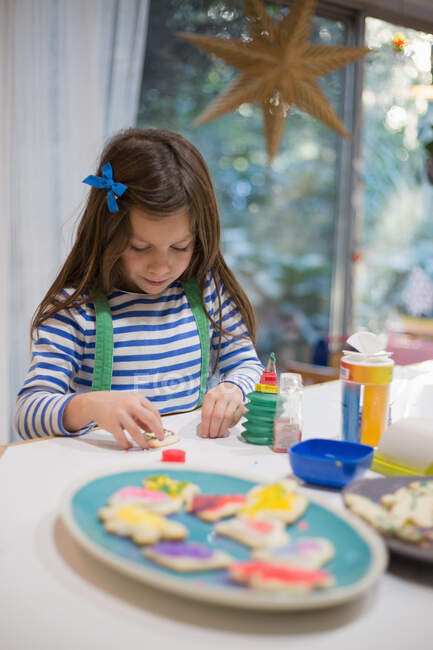 Девушка украшает рождественское печенье для тарелки на кухонном столе — стоковое фото