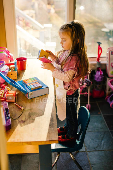 Girl standing on playroom chair reading storybook — Stock Photo