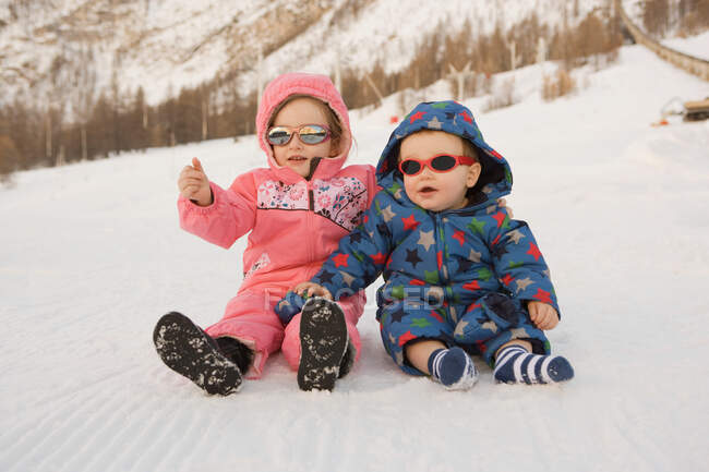 Retrato de irmão e irmã sentados na neve — Fotografia de Stock