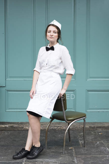 Mujer vistiendo uniforme de camarera, apoyada en la silla - foto de stock