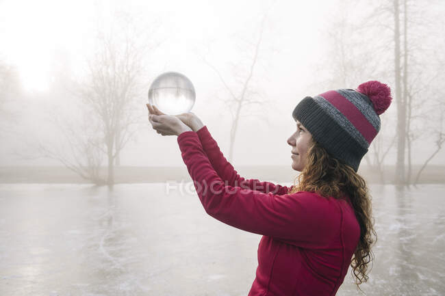 Woman holding up crystal ball on frozen lake — Stock Photo