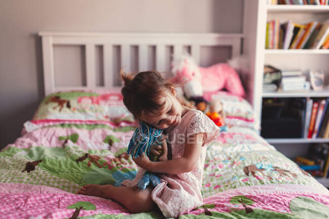 Дівчина сидить на ліжку обіймає ганчірку ляльку — стокове фото