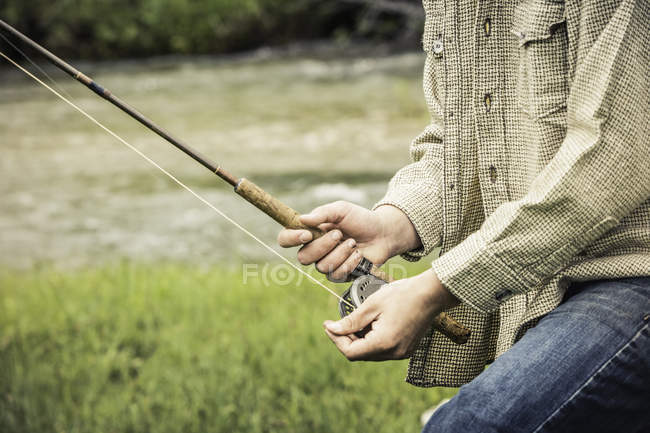 Vue recadrée du jeune homme enroulant bobine de pêche sur la canne à pêche — Photo de stock