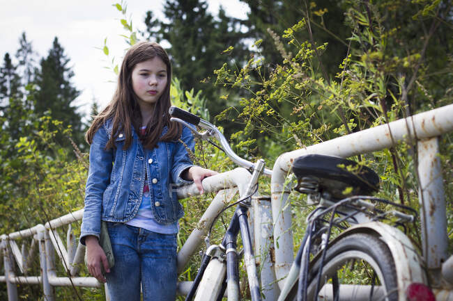 Дівчина-підліток дивиться на свій велосипед на сільській дорозі — стокове фото
