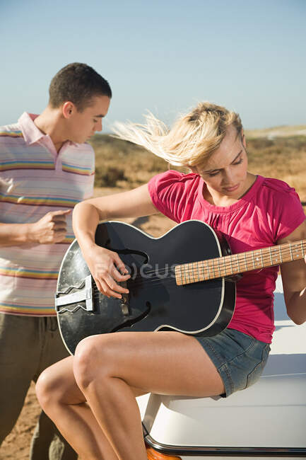 A young woman playing a guitar and a young man — Stock Photo