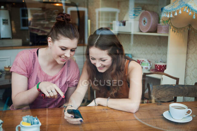 Young women in cafe looking at cell phone — Stock Photo