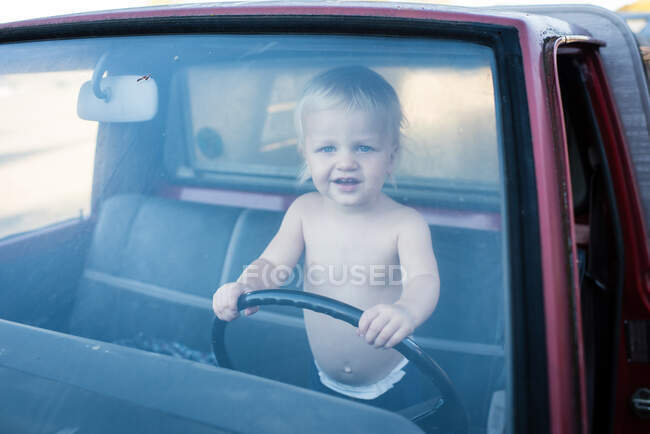 Portrait of male toddler standing in truck holding steering wheel — Stock Photo