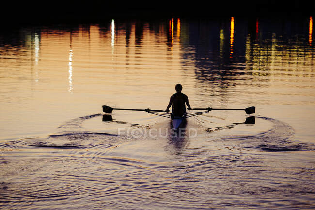 Jeune homme ramant sur la rivière au coucher du soleil — Photo de stock