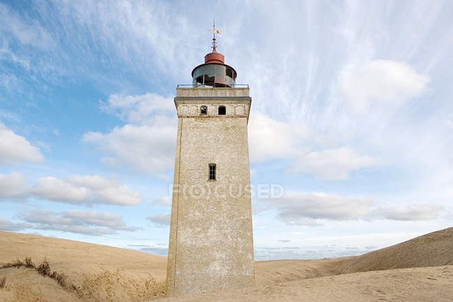 Bâtiment phare sur la plage de sable avec ciel nuageux bleu — Photo de stock