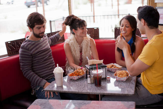 Cuatro amigos sentados juntos en la cafetería, sonriendo - foto de stock