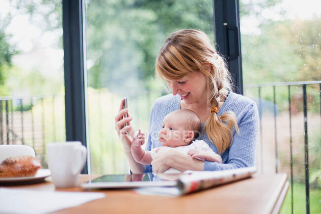 Mother with cell phone and newborn daughter — Stock Photo