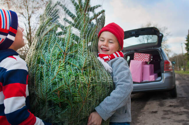 Two boys lifting Christmas tree to car — Stock Photo